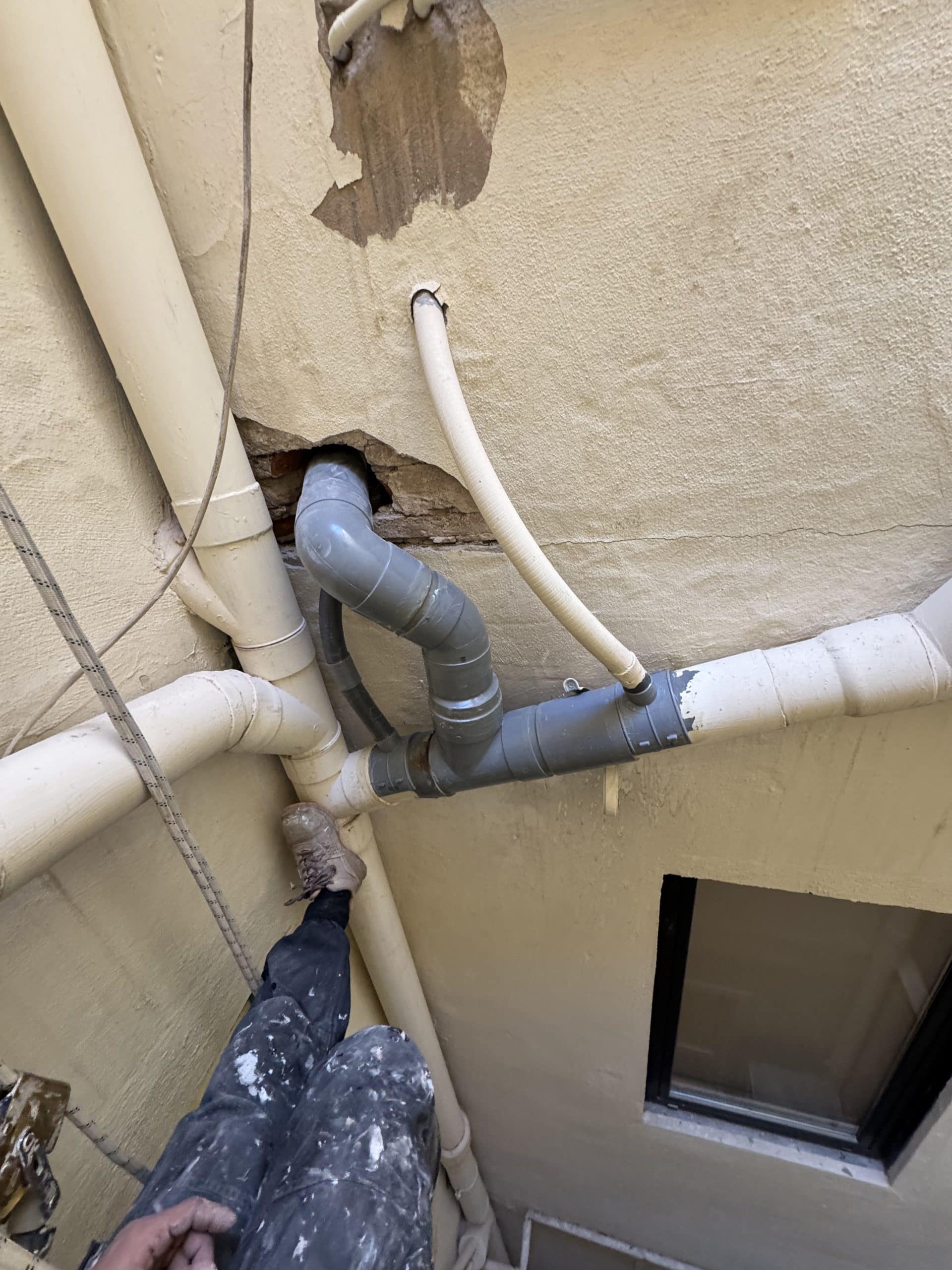 Conexión de bajante con tramo gris y tubería horizontal en un patio